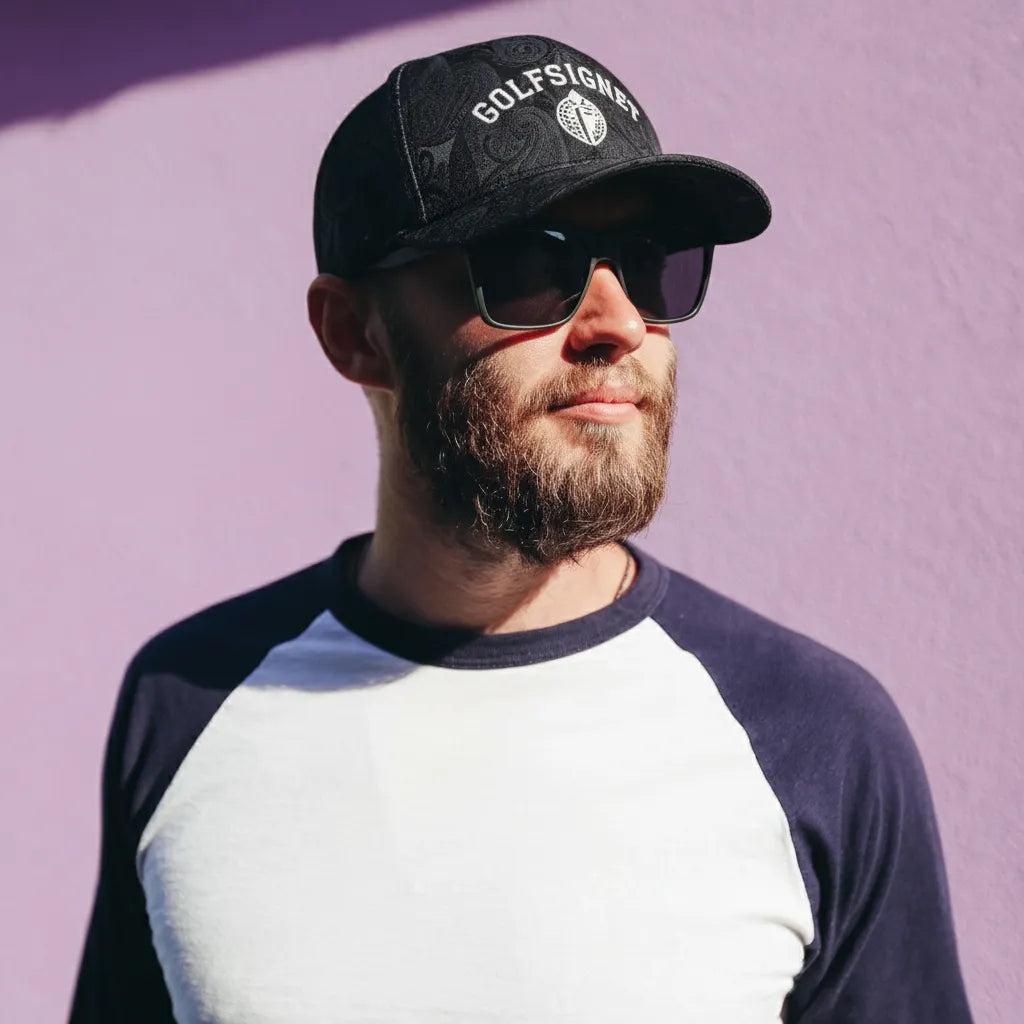 Man wearing a black cap and sunglasses with a purple background
