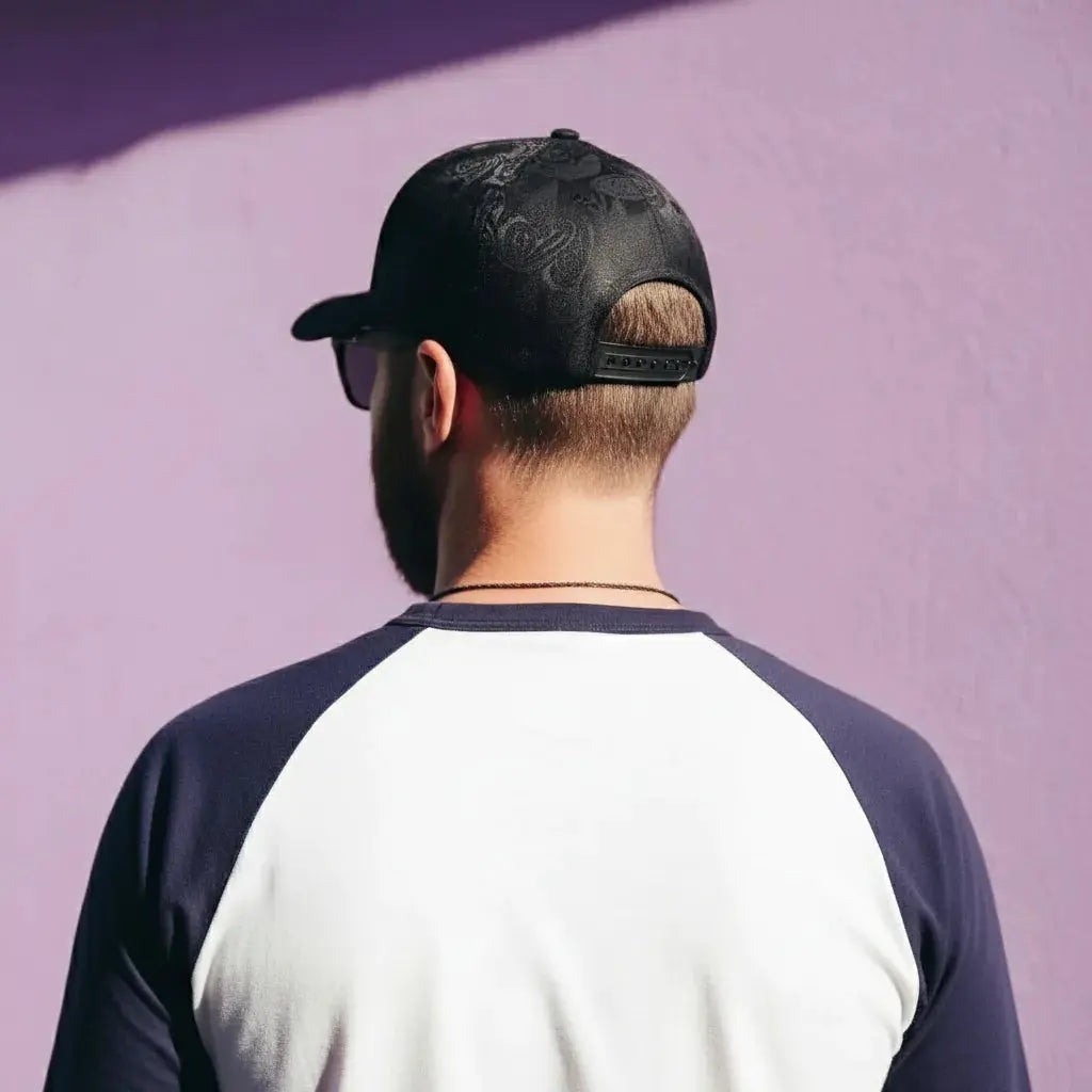 Person wearing a black cap and a two-tone shirt against a purple wall