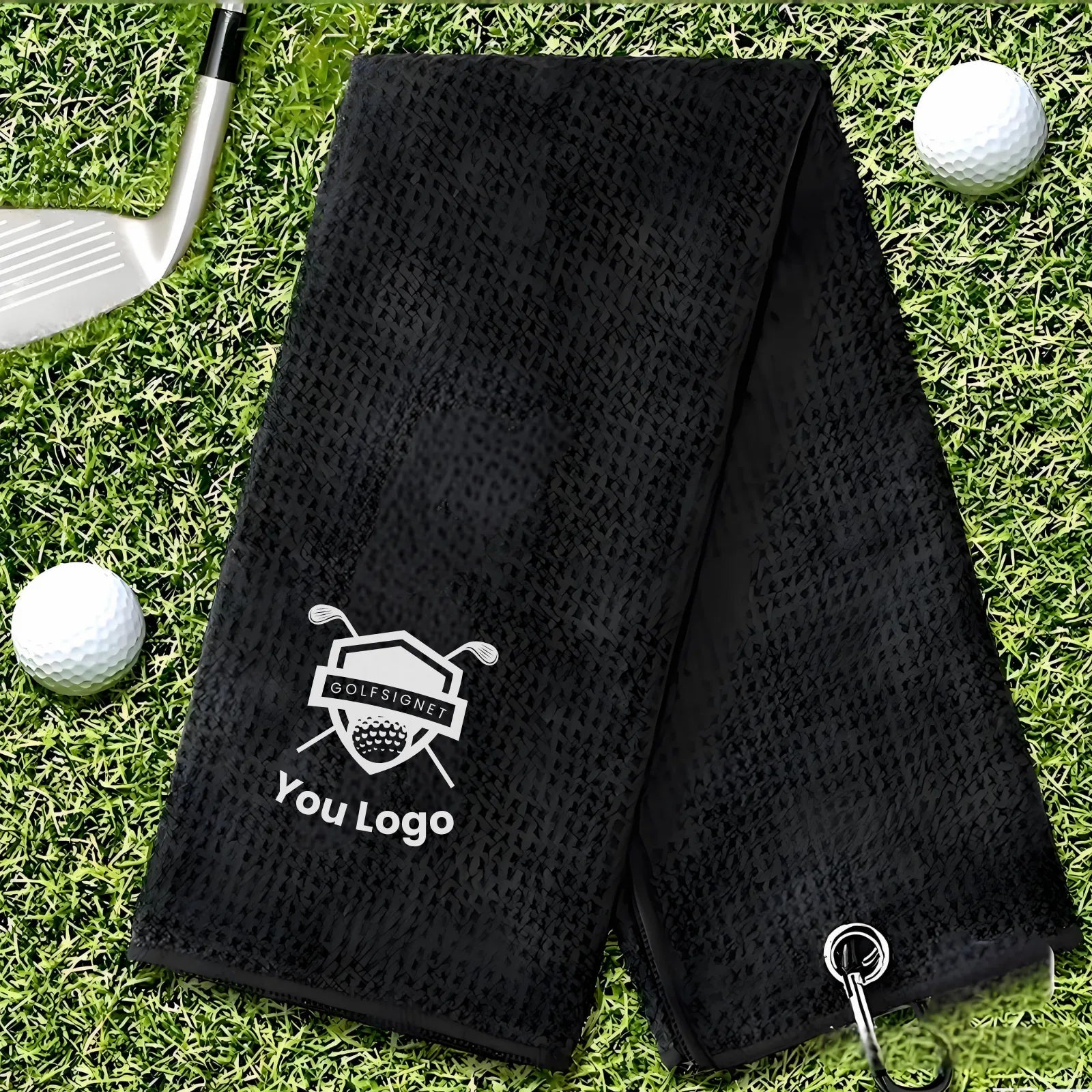 Black perforated golf towel with a logo on grass with golf balls and club