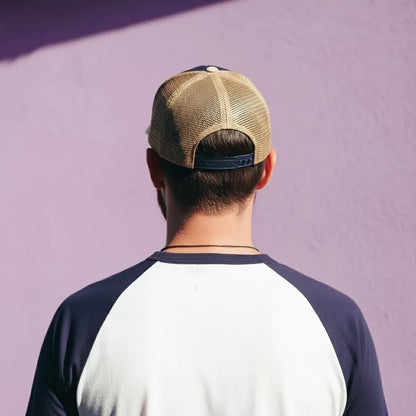 Person wearing a beige and navy cap and a two-tone shirt against a purple wall