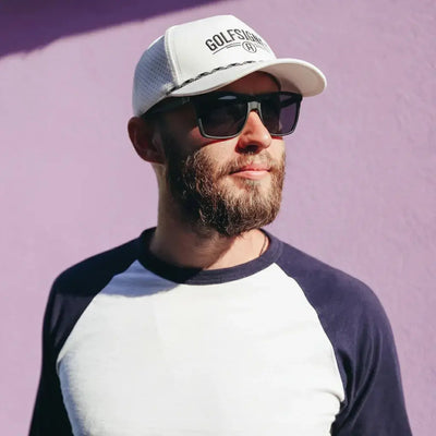 Man wearing a cap and sunglasses against a purple background