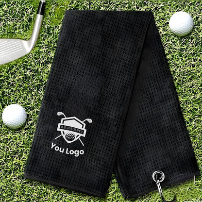 Black perforated golf towel with a logo on grass with golf balls and club